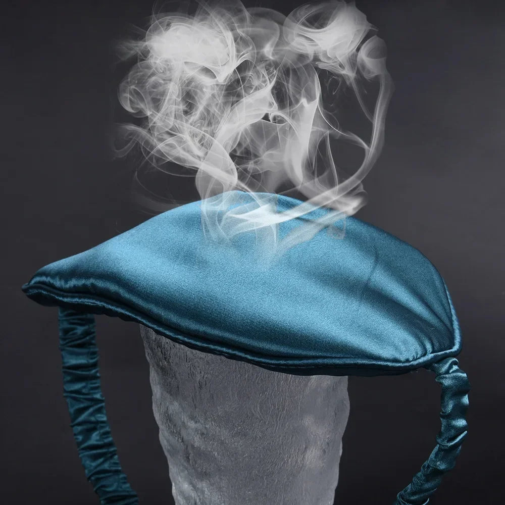 A teal silk sleep mask is shown resting on a white mannequin, with wisps of smoke rising above it.