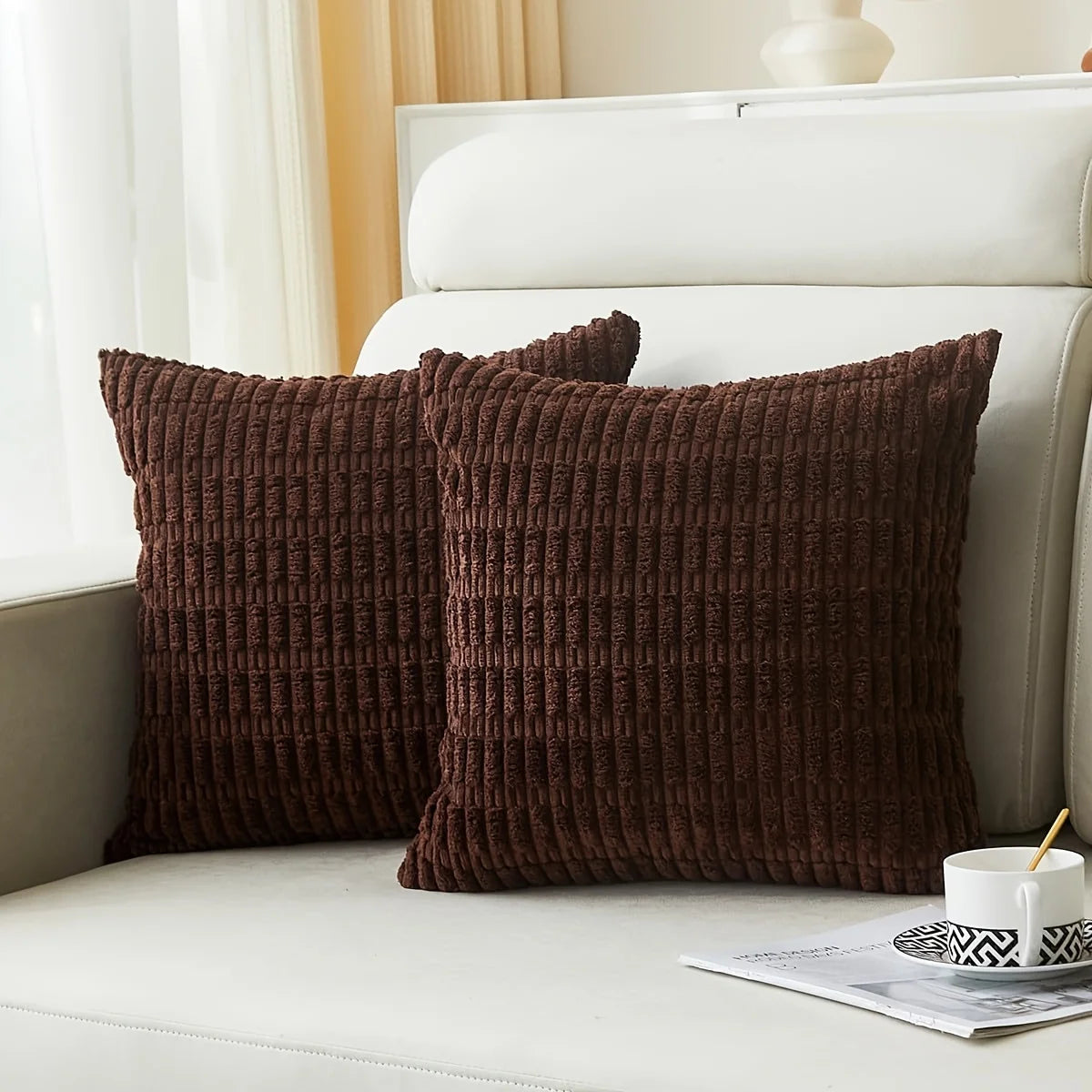 A dark brown corduroy decorative throw pillow cover with a vertical stripe design resting on a white bed.