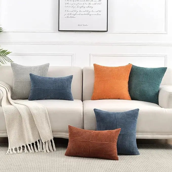 A collection of retro corduroy patchwork pillow covers in various shades of blue, orange, and gray displayed on a sofa.