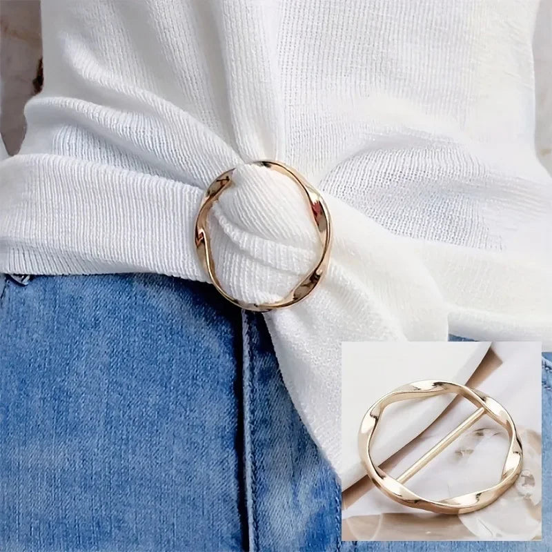 A gold metal round clip buckle is shown against a white knitted sweater and denim fabric.