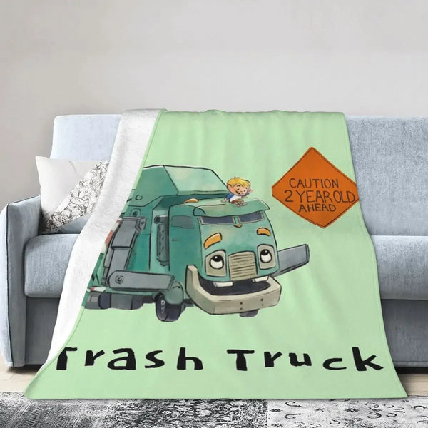 A cartoon illustration of a green trash truck on a light green background printed on a flannel throw blanket.