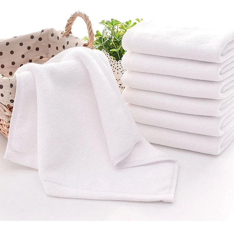 A stack of ten white cotton face towels is shown next to a folded towel on a white surface.