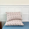 A set of two plaid fabric pillow covers in beige and brown tones resting on a blue surface.
