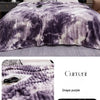 A purple and white tie-dye flannel fleece throw blanket draped over a bed.