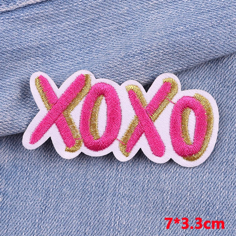 Pink and gold embroidered letter patches spelling XOXO on a denim fabric background