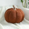A round, fuzzy brown pumpkin plush decoration resting on a white textured fabric.