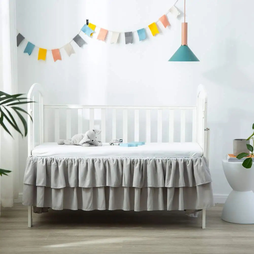 A white crib with a ruffled gray bed skirt and a teal pendant light hanging above it in a bright nursery room.