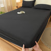 A dark gray fitted bed sheet set is laid out on a wooden bed with pillows and a cup on the sheet.