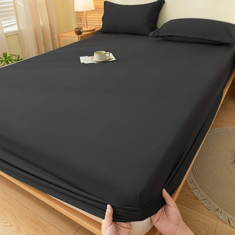 A dark gray fitted bed sheet set is laid out on a wooden bed with pillows and a cup on the sheet.