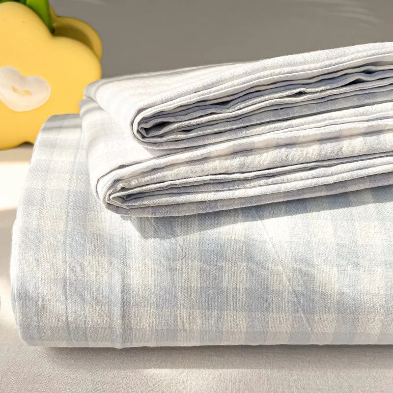 A stack of light blue and white plaid organic cotton bedding sheets and pillowcases on a surface.