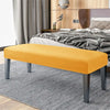 A bright orange velvet bench slipcover with secure straps placed on a gray striped rug in a bedroom setting.