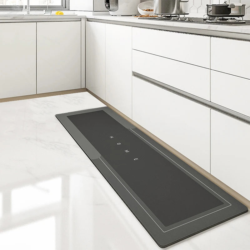 A rectangular gray non-slip floor mat is placed on a white marble kitchen floor next to white cabinetry.