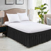 A white bed with a black elastic bed skirt and neutral bedding in a bedroom setting.