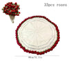 A round white knitted floral blanket with a red border and a small bouquet of red roses.