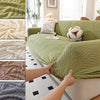 Close-up view of a sage green stretch sofa cover with an elegant plant pattern texture and elastic edge.