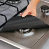 A hand places a black reusable gas hob protector liner onto a stovetop burner.