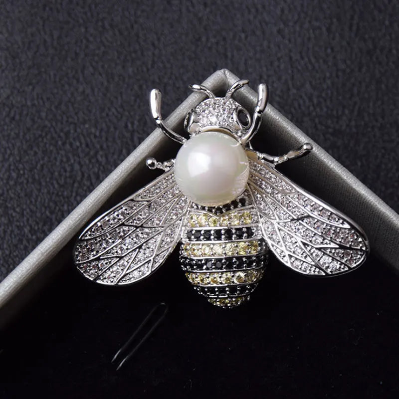 A silver and diamond crystal bee brooch featuring a pearl accent on the body and detailed wings.