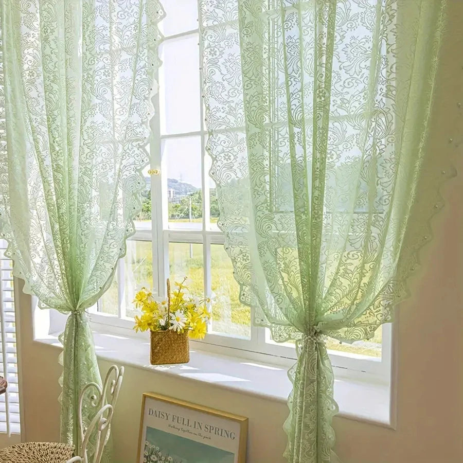 Light green lace curtain with beaded phoenix tail design hanging over a window.