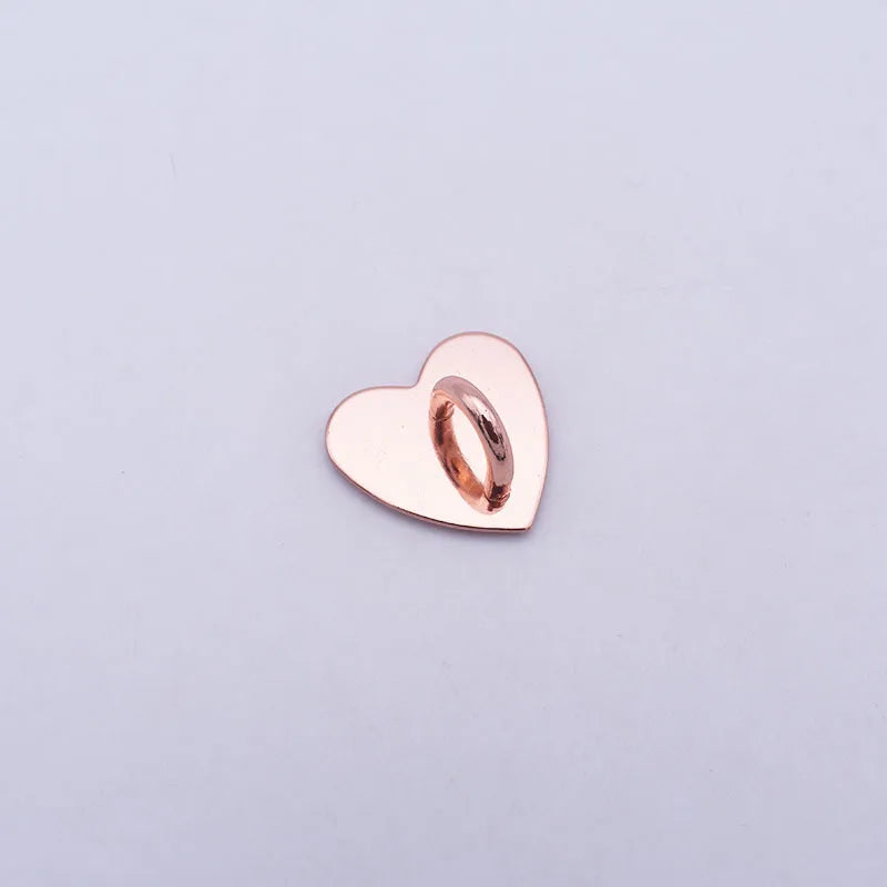 A small, rose gold heart-shaped metal charm used as a phone accessory or connector.