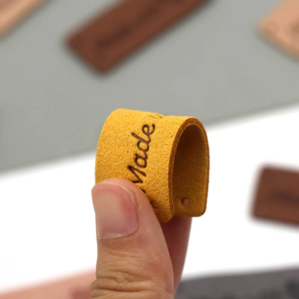 A hand holds a yellow felt tag with the word Made stamped on it.