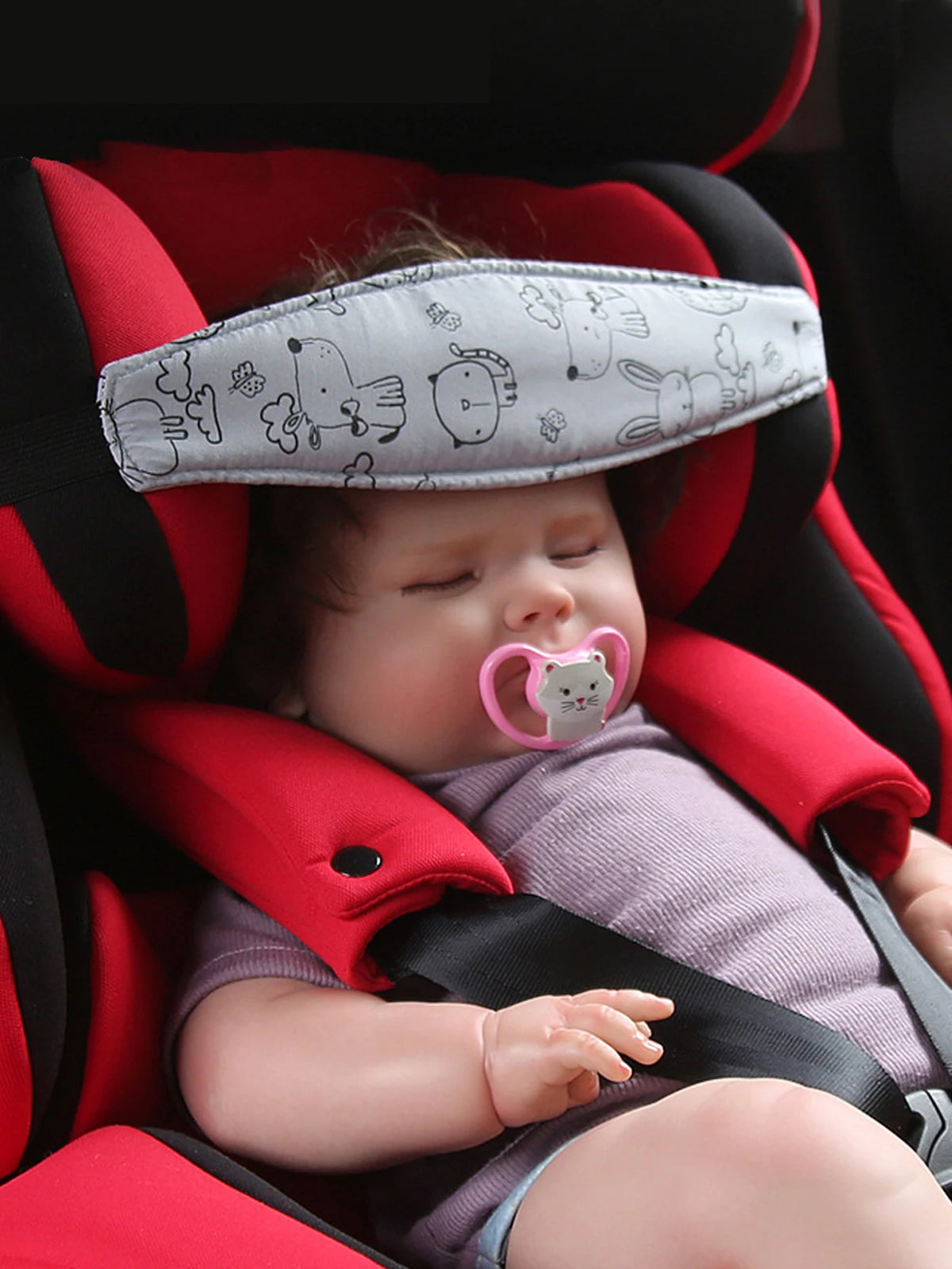 A baby is resting in a red car seat with a gray head support pillow.