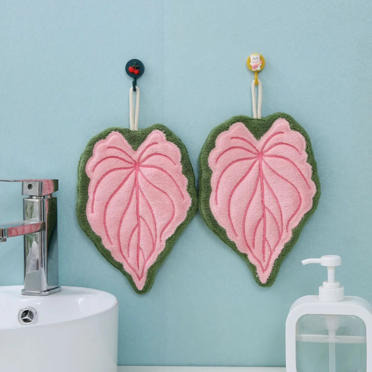 Two heart-shaped hand towels with pink and green leaves hanging on a light blue wall.