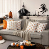 A gray sofa decorated with white and orange pumpkin throw pillows and a beige throw blanket.