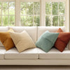 A set of four neutral corduroy throw pillow covers with a patchwork design displayed on a white sofa.