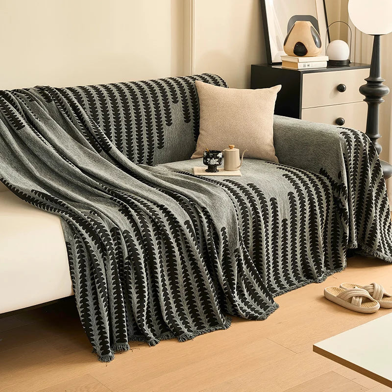 A charcoal gray herringbone chenille sofa cover with black and white patterned tassels draped over a sofa.