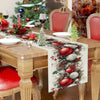 A linen table runner featuring Christmas pine cones and red berries on a wooden dining table.