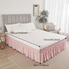 White bed with a pink ruffled elastic skirt and light gray headboard in a bedroom setting