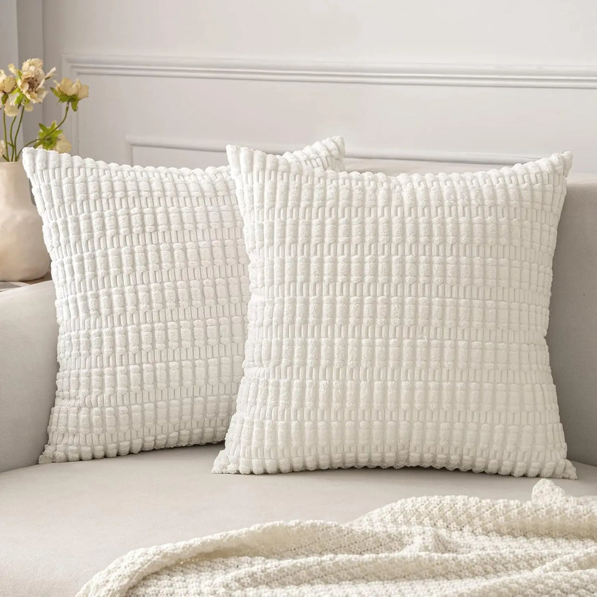 A white textured corduroy throw pillow cover displayed on a sofa with a white headboard and a cream blanket.