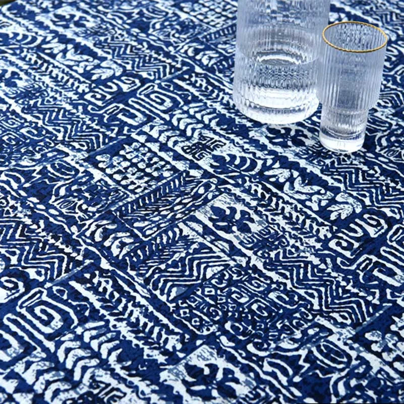 A close-up of a navy blue and white bohemian printed linen fabric spread on a surface with a glass.