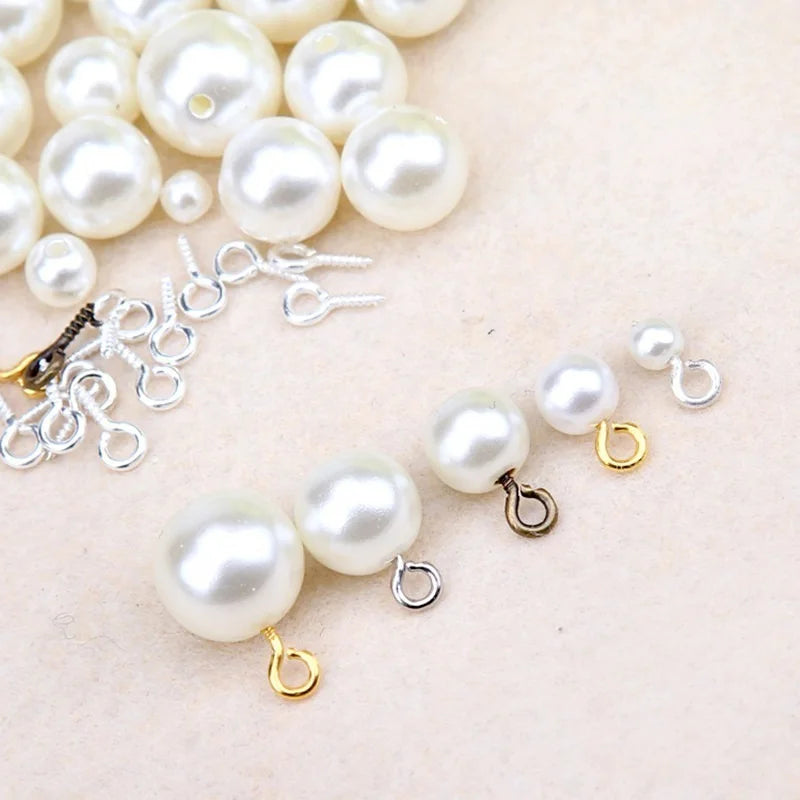 A collection of small, round, off-white pearl beads and silver eye screw pins for jewelry making.