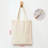 A beige reusable canvas tote bag hanging from a wooden hanger, showing its size and strap detail.