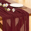 A deep burgundy cheesecloth table runner decorated with white flowers and a silver fork on a wooden table.