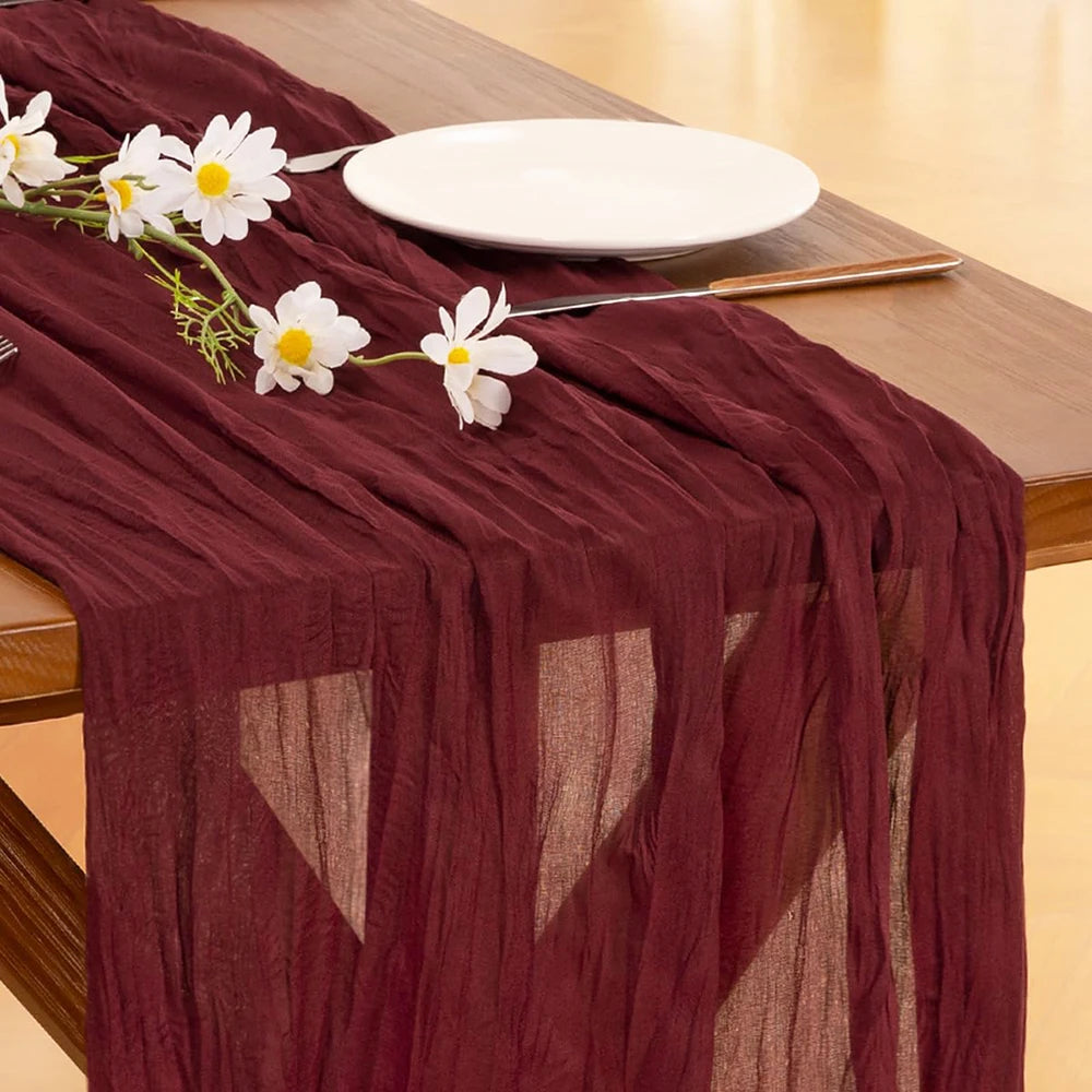 A deep burgundy cheesecloth table runner decorated with white flowers and a silver fork on a wooden table.