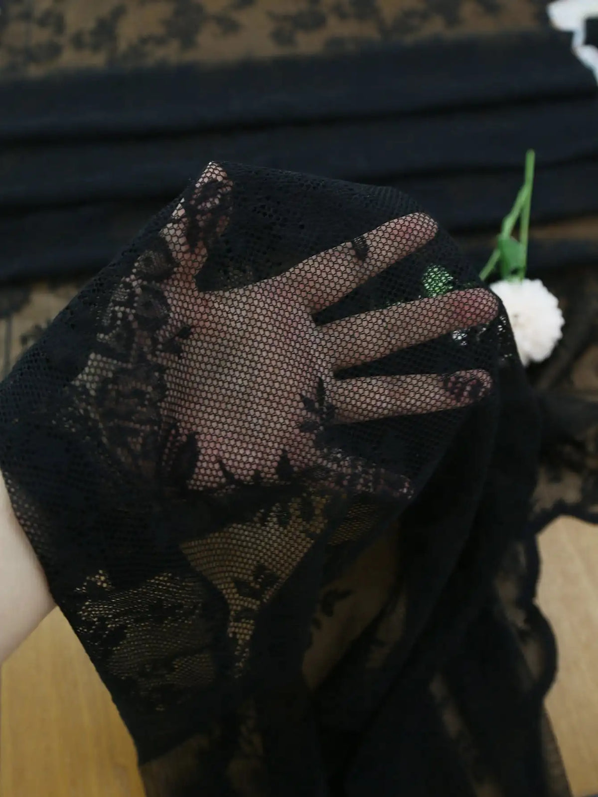 Black floral lace sheer fabric with a mesh hand, displayed against a dark background.