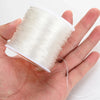 A hand holds a spool of transparent elastic cord used for jewelry making.