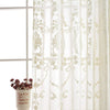 Sheer white curtains with delicate floral embroidery hanging in a window.