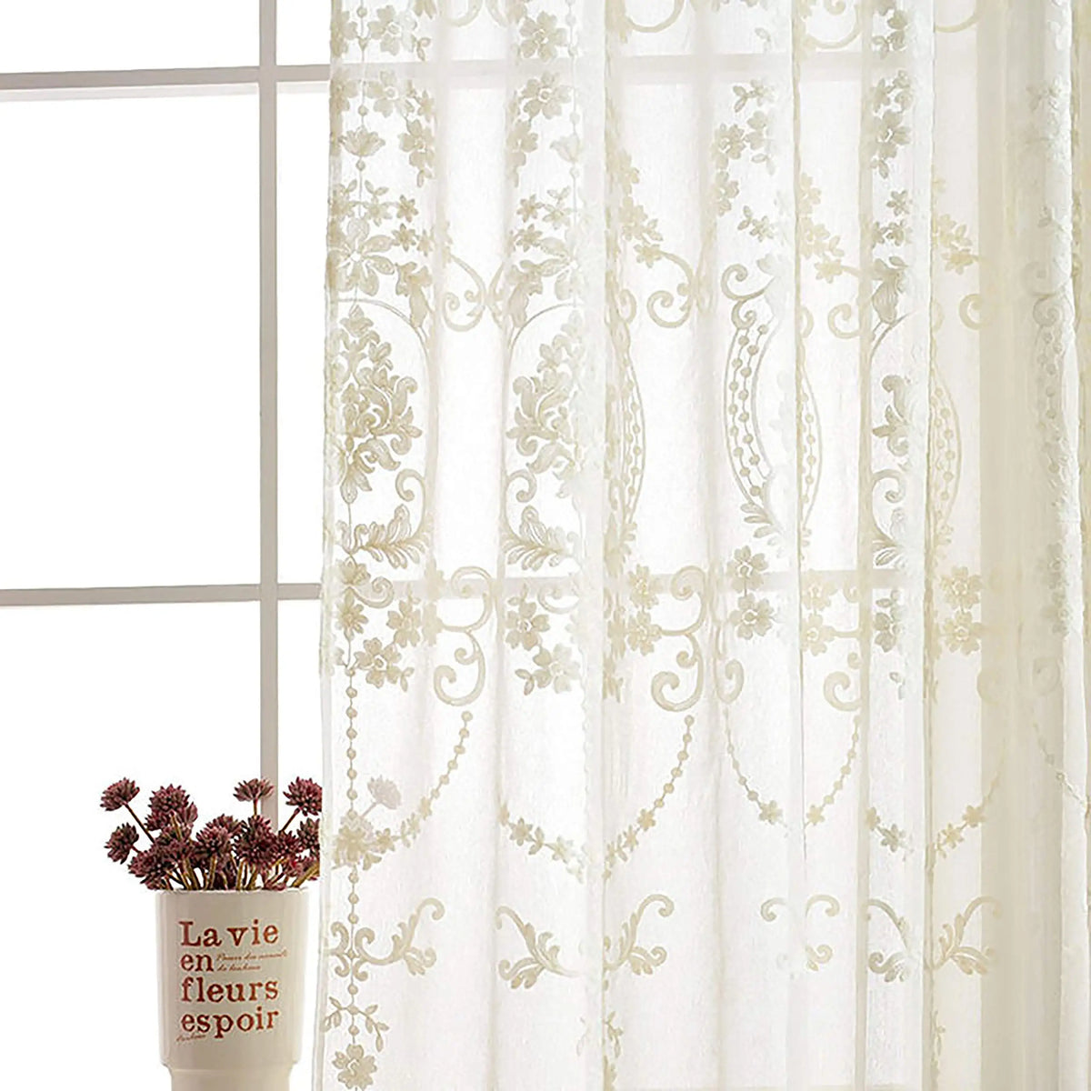 Sheer white curtains with delicate floral embroidery hanging in a window.