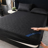 A black quilted mattress protector is shown on a bed, with a hand touching the fabric.