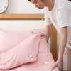 A person is adjusting a pink quilt with small white silicone clips on a wooden bed frame.