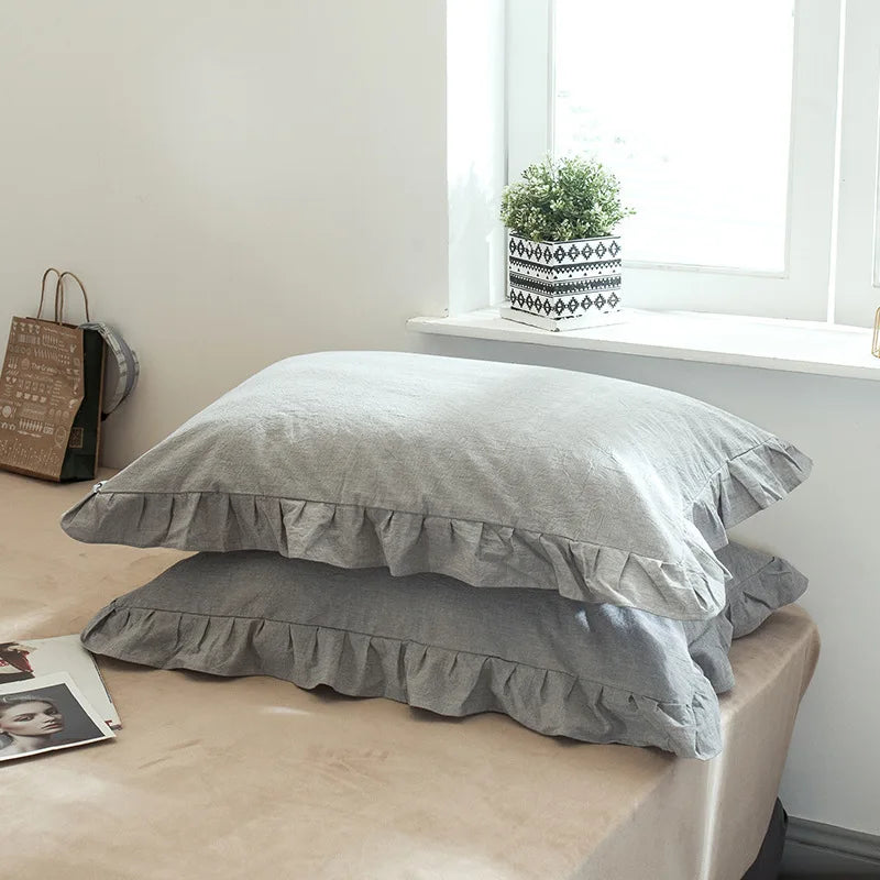 A set of two soft plaid washed cotton pillowcases with ruffled edges resting on a light-colored table.