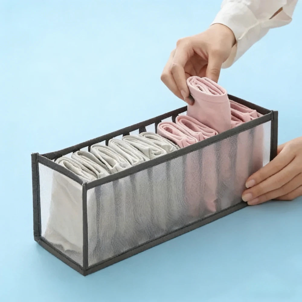 A hand is placing pink folded undergarments into a black drawer organizer box.