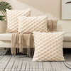 A collection of cream-colored, textured plush pillows arranged on a light sofa and a gray patterned floor.