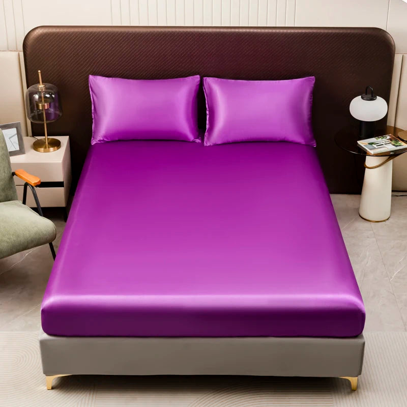 A purple satin bedding set with fitted sheets displayed on a bed with brown headboard and pillows.