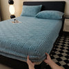 A teal plush jacquard mattress cover is shown on a bed, with pillows and a decorative object nearby.