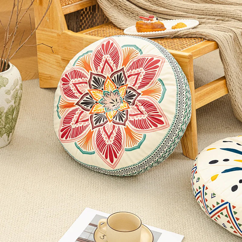 A round cushion with a colorful, mandala-like floral pattern is placed on a wooden floor frame.
