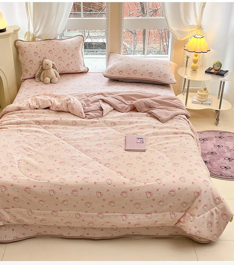 A pink cartoon quilting comforter is displayed on a bed with white curtains and a yellow lamp.